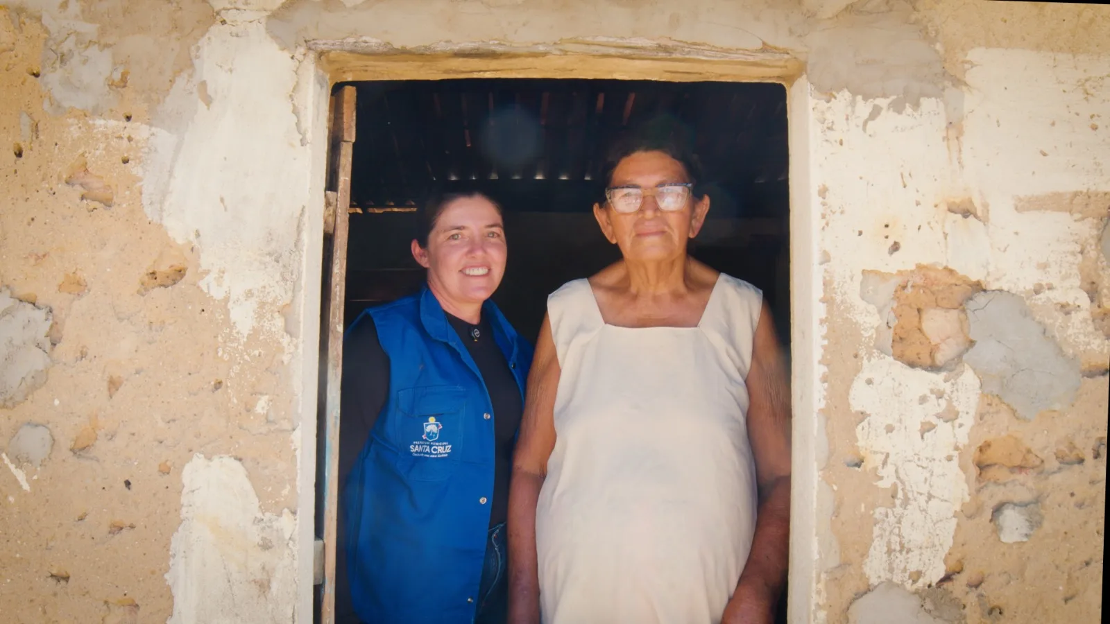 Agente comunitária de saúde ao lado de uma moradora na porta de casa